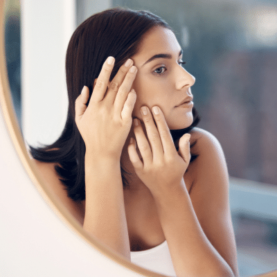 Woman checking the side of her face in a mirror, representing how to check for skin cancer at home